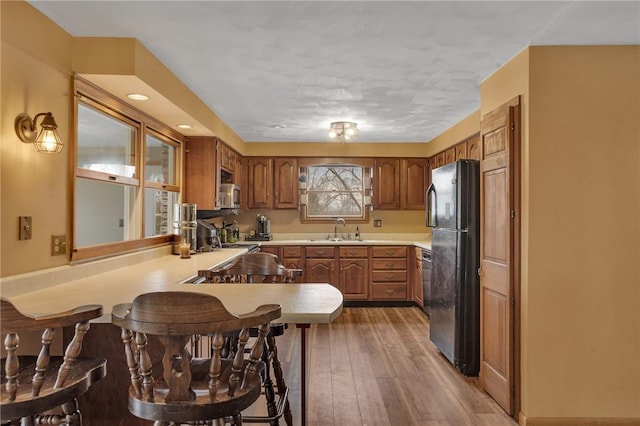 kitchen with a peninsula, wood finished floors, a sink, freestanding refrigerator, and stainless steel microwave