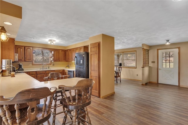 kitchen with a sink, light countertops, freestanding refrigerator, brown cabinets, and light wood finished floors