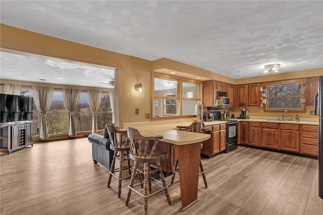 kitchen with light countertops, stainless steel microwave, electric range, brown cabinetry, and a sink