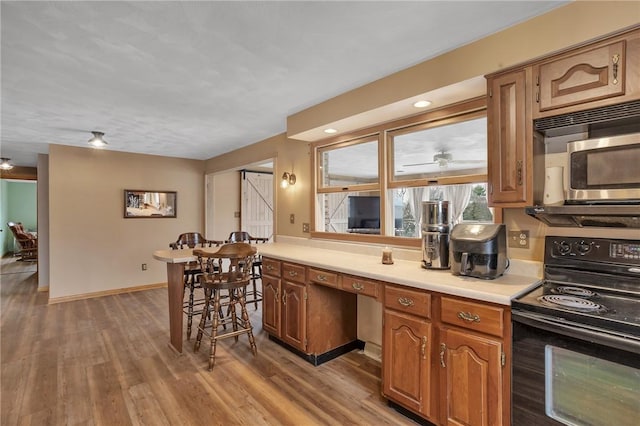 kitchen with electric range, baseboards, light wood-style flooring, brown cabinets, and light countertops