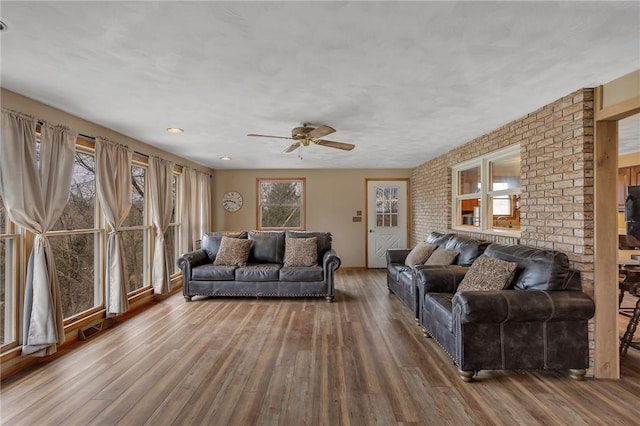 living room featuring a ceiling fan, visible vents, brick wall, and wood finished floors