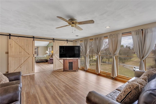 living area with light wood-type flooring, ceiling fan, and a barn door