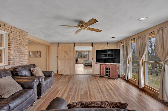 living room featuring a barn door, light wood-style flooring, and a ceiling fan