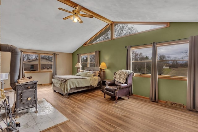 bedroom featuring vaulted ceiling with beams, light wood-style flooring, visible vents, baseboards, and a wood stove