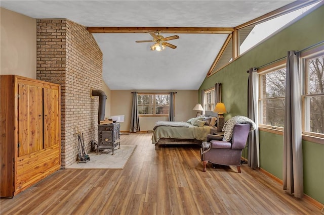 bedroom with a wood stove, multiple windows, beam ceiling, and wood finished floors