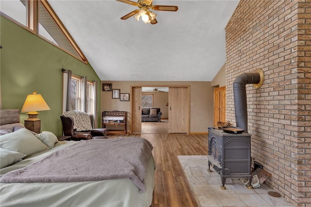 bedroom with baseboards, high vaulted ceiling, a wood stove, and light wood-style floors