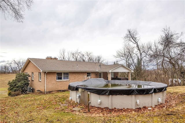 rear view of property with central AC, brick siding, a chimney, and a covered pool