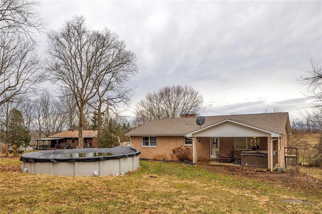 rear view of house with a deck, brick siding, a yard, a covered pool, and a chimney