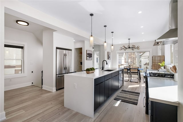 kitchen featuring wall chimney exhaust hood, appliances with stainless steel finishes, dark cabinets, light countertops, and a sink