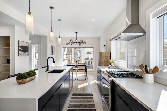 kitchen with dark cabinets, a sink, stainless steel gas range oven, and wall chimney exhaust hood