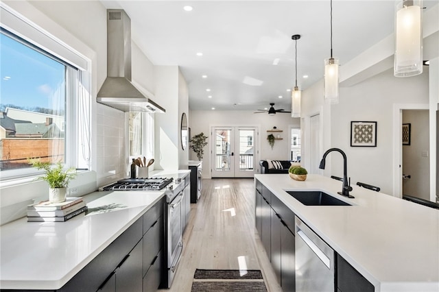 kitchen featuring a sink, appliances with stainless steel finishes, french doors, wall chimney exhaust hood, and modern cabinets