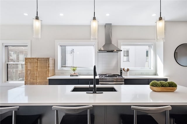 kitchen with light countertops, a sink, wall chimney range hood, and a kitchen bar