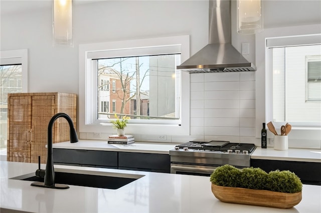 kitchen featuring a sink, light countertops, wall chimney range hood, backsplash, and stainless steel gas stove