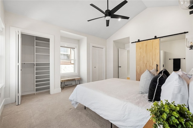 bedroom featuring lofted ceiling, a barn door, light carpet, a ceiling fan, and multiple closets