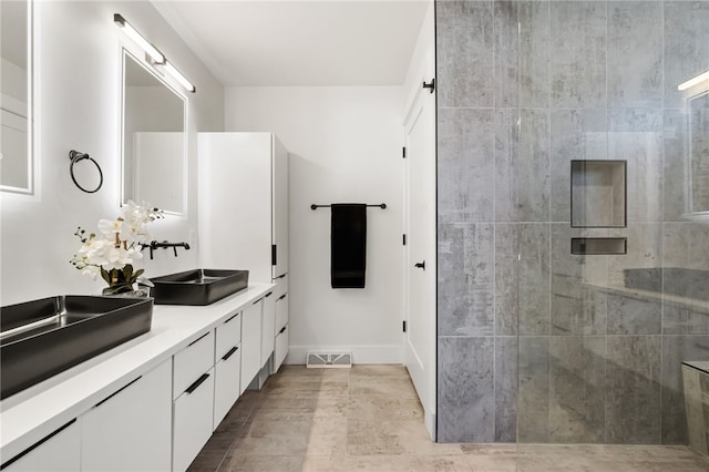 bathroom featuring double vanity, a stall shower, baseboards, visible vents, and a sink