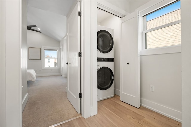 laundry area with light wood-type flooring, stacked washer and dryer, baseboards, and laundry area