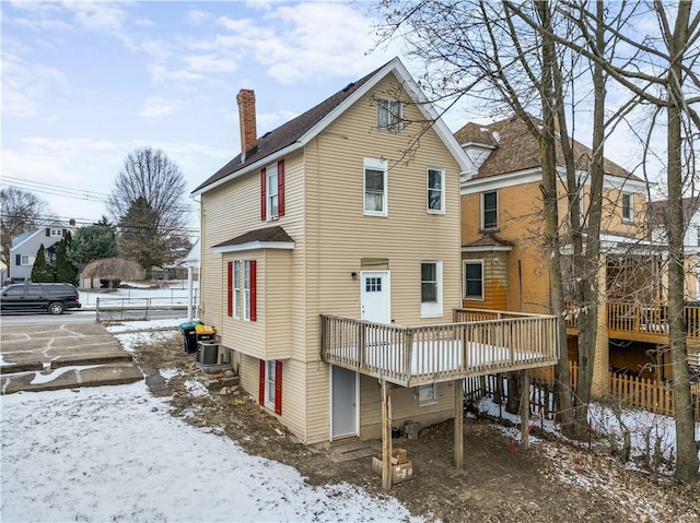 snow covered rear of property with a chimney, cooling unit, and a wooden deck