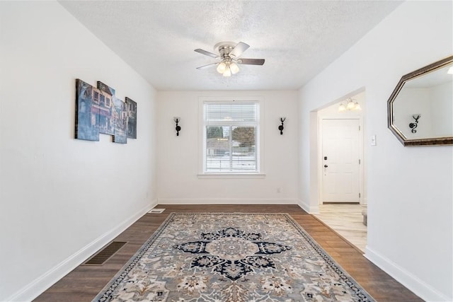 interior space featuring a textured ceiling, dark wood-style flooring, visible vents, and baseboards