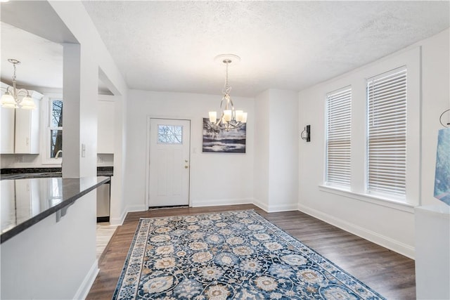 foyer with an inviting chandelier, a textured ceiling, baseboards, and dark wood-type flooring