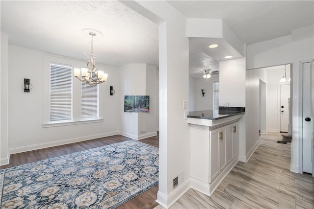 kitchen with light wood finished floors, visible vents, baseboards, dark countertops, and ceiling fan with notable chandelier