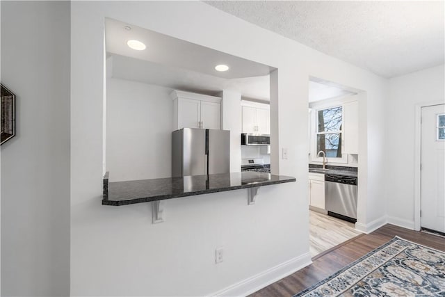 kitchen with appliances with stainless steel finishes, a kitchen breakfast bar, light wood-style floors, white cabinetry, and a sink