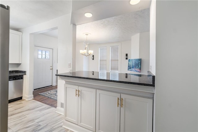 kitchen featuring white cabinetry, a textured ceiling, dark stone countertops, dishwasher, and a peninsula