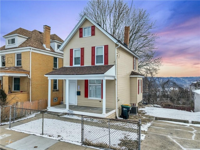 traditional-style home with a fenced front yard, a chimney, a porch, and central AC