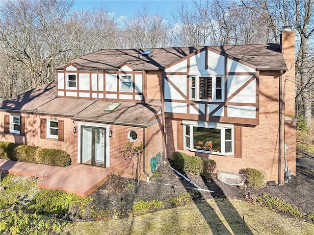 english style home with roof with shingles, a chimney, and brick siding