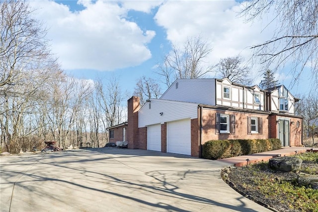 view of side of home featuring a garage, brick siding, driveway, and a chimney