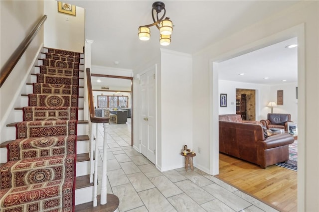 foyer entrance featuring stairs, ornamental molding, light wood-type flooring, and a notable chandelier