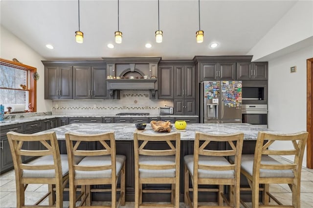 kitchen with dark brown cabinetry, tasteful backsplash, lofted ceiling, light stone counters, and stainless steel appliances