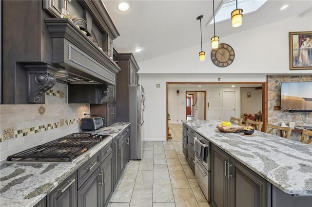 kitchen featuring light stone counters, stainless steel appliances, vaulted ceiling, hanging light fixtures, and decorative backsplash