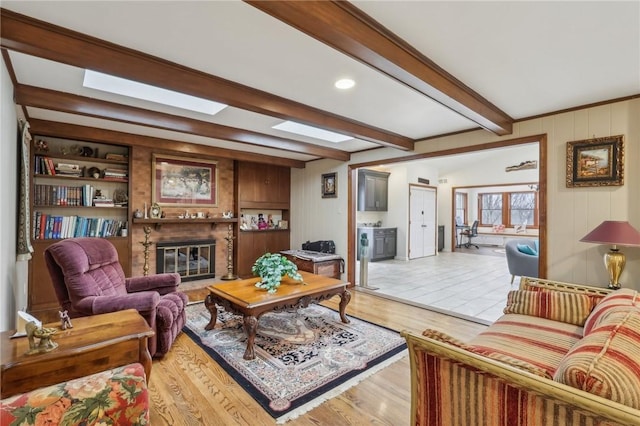 living room featuring wood walls, a skylight, beam ceiling, light wood finished floors, and a glass covered fireplace