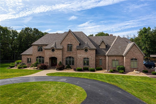 french provincial home featuring brick siding, roof with shingles, a chimney, fence, and a front lawn