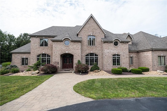 french provincial home featuring a front yard, brick siding, driveway, and roof with shingles