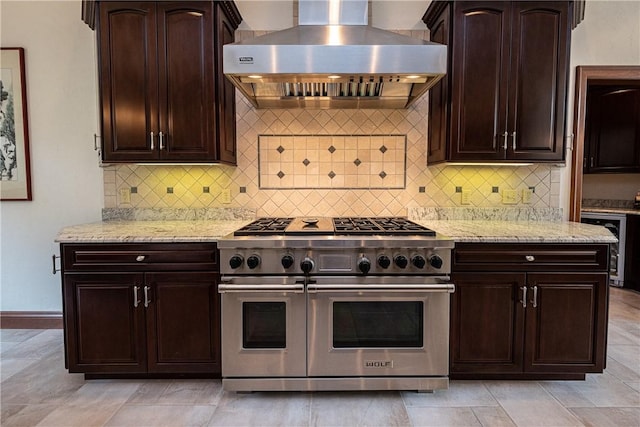 kitchen featuring range with two ovens, backsplash, dark brown cabinetry, wall chimney range hood, and light stone countertops