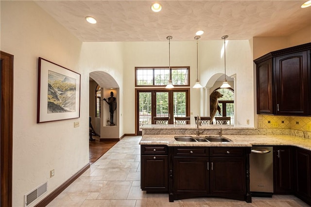 kitchen with arched walkways, visible vents, decorative backsplash, a sink, and light stone countertops