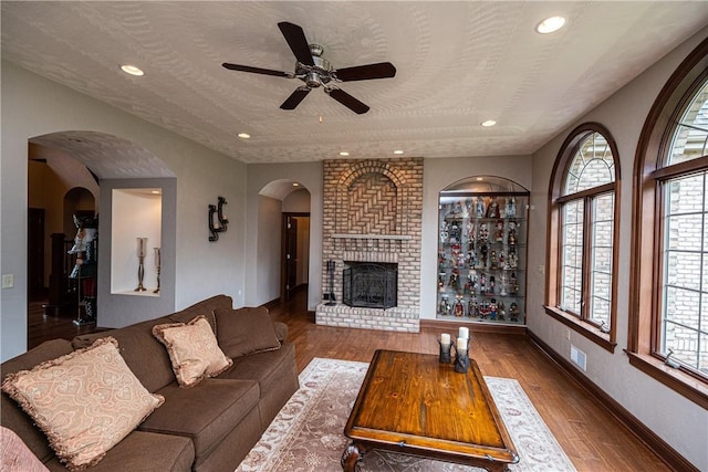 living area featuring a textured ceiling, a brick fireplace, wood finished floors, and baseboards