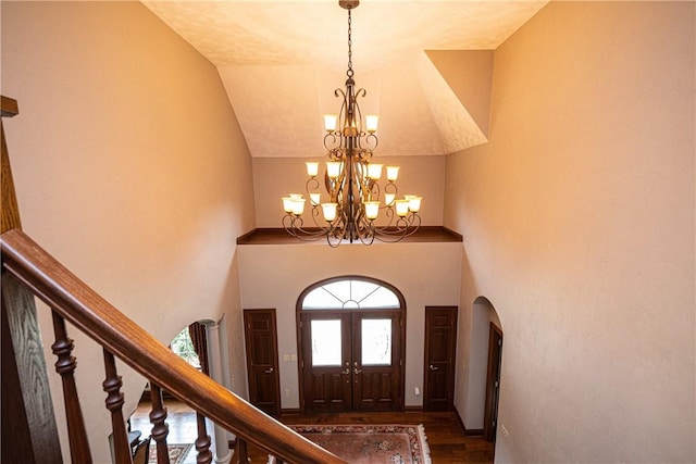 foyer entrance with a chandelier, arched walkways, high vaulted ceiling, and stairway