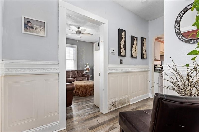 interior space with a textured ceiling, a wainscoted wall, wood finished floors, visible vents, and a ceiling fan