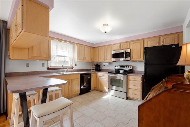 kitchen with a breakfast bar area, a peninsula, a sink, light brown cabinetry, and black appliances