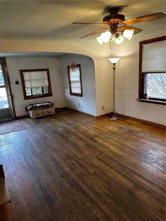 unfurnished living room featuring arched walkways, dark wood finished floors, baseboards, and ceiling fan