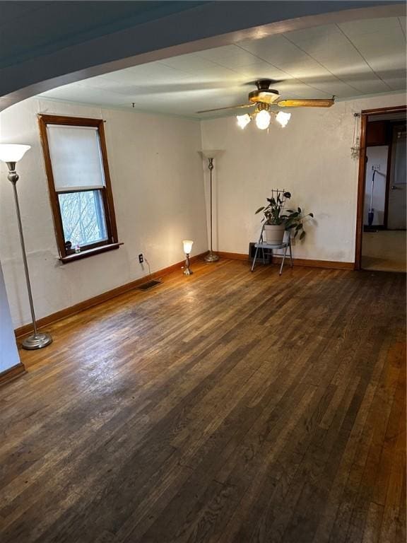 unfurnished room with dark wood-style floors, visible vents, baseboards, and a ceiling fan