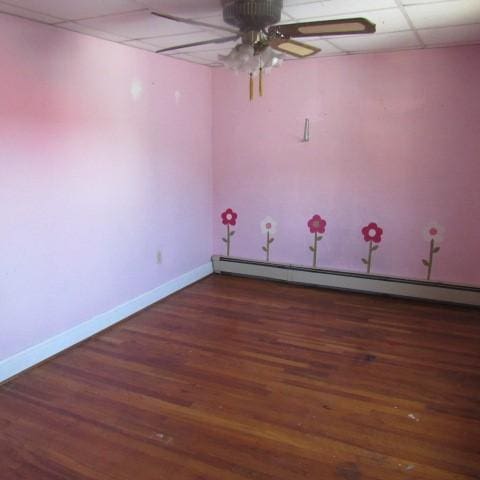 empty room with a baseboard radiator, baseboards, a drop ceiling, and wood finished floors