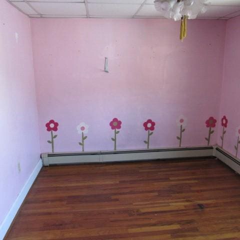 empty room with baseboard heating, a drop ceiling, wood finished floors, and baseboards