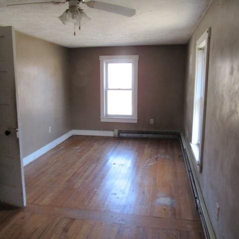 unfurnished room featuring ceiling fan, baseboard heating, wood finished floors, and baseboards