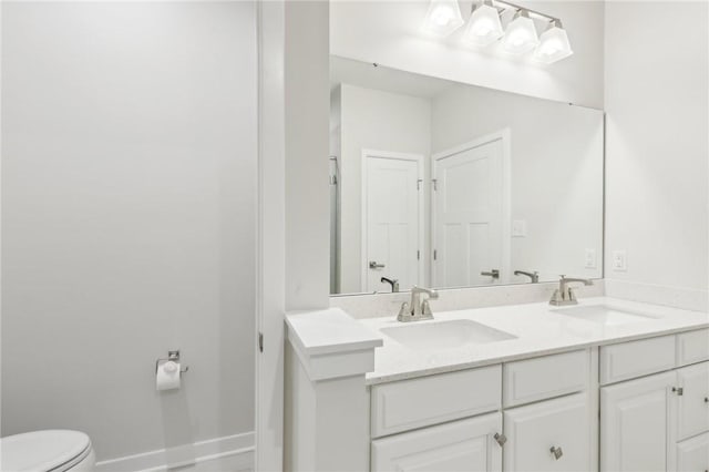 full bath with double vanity, a sink, toilet, and baseboards