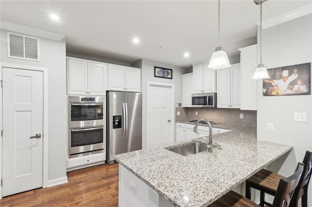 kitchen with visible vents, a peninsula, stainless steel appliances, white cabinetry, and a sink