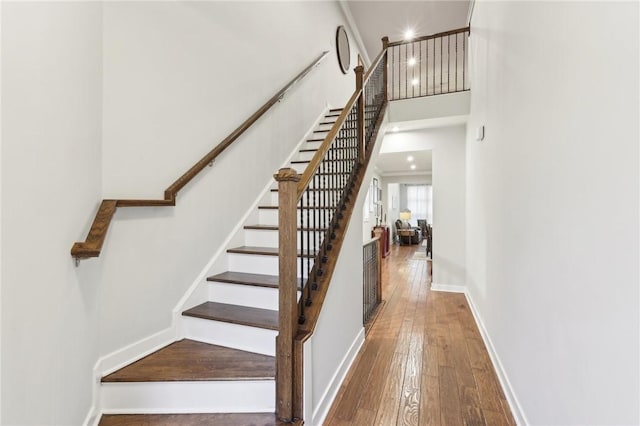 stairway with hardwood / wood-style flooring, a high ceiling, and baseboards