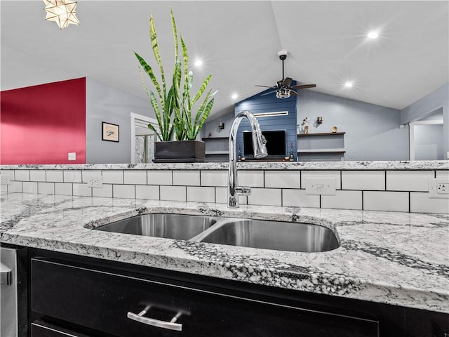 kitchen with a ceiling fan, lofted ceiling, light stone counters, dark cabinets, and a sink